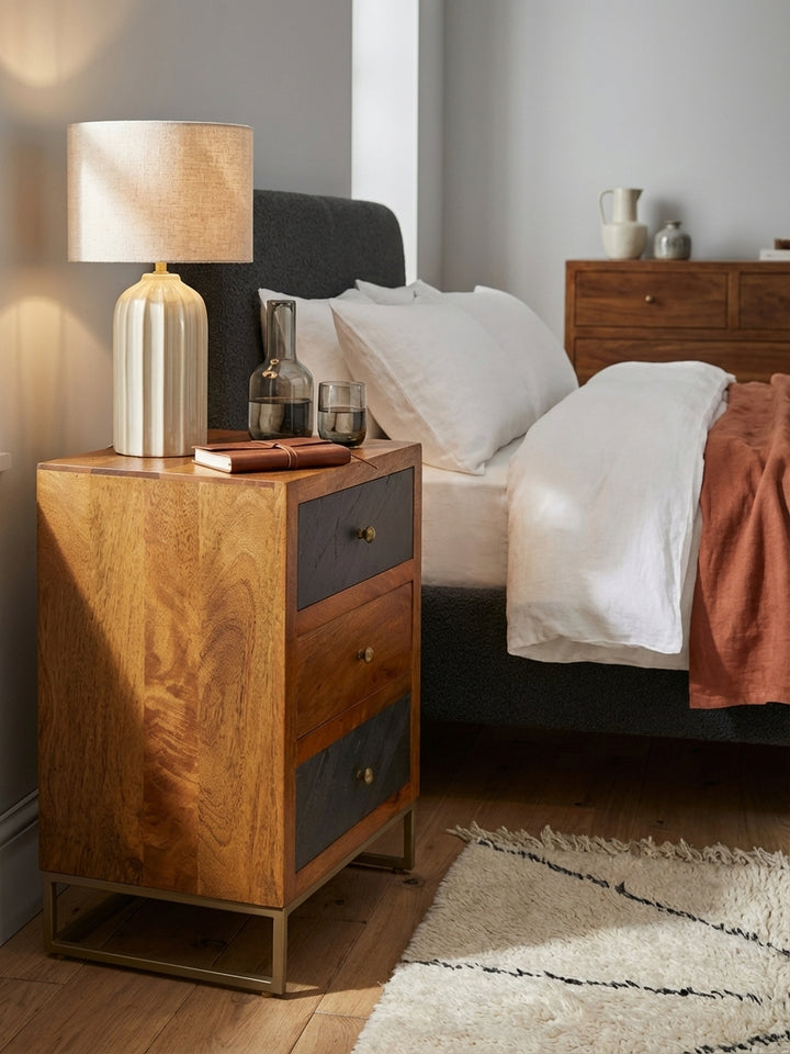 Ein Glas Wasser und eine Design-Tischlampe stehen auf dem braunen Nachttisch aus Mangoholz, der eine gemütliche Atmosphäre im modernen Schlafzimmer schafft._