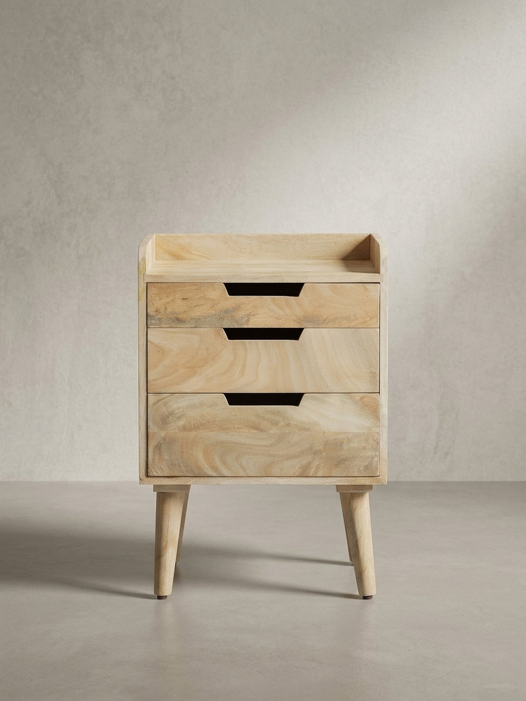 Schräge 3/4-Ansicht der Nachtkommode, die die Tiefe der grifflosen Schubladen und die schlanke Silhouette des Massivholzmöbels zeigt._