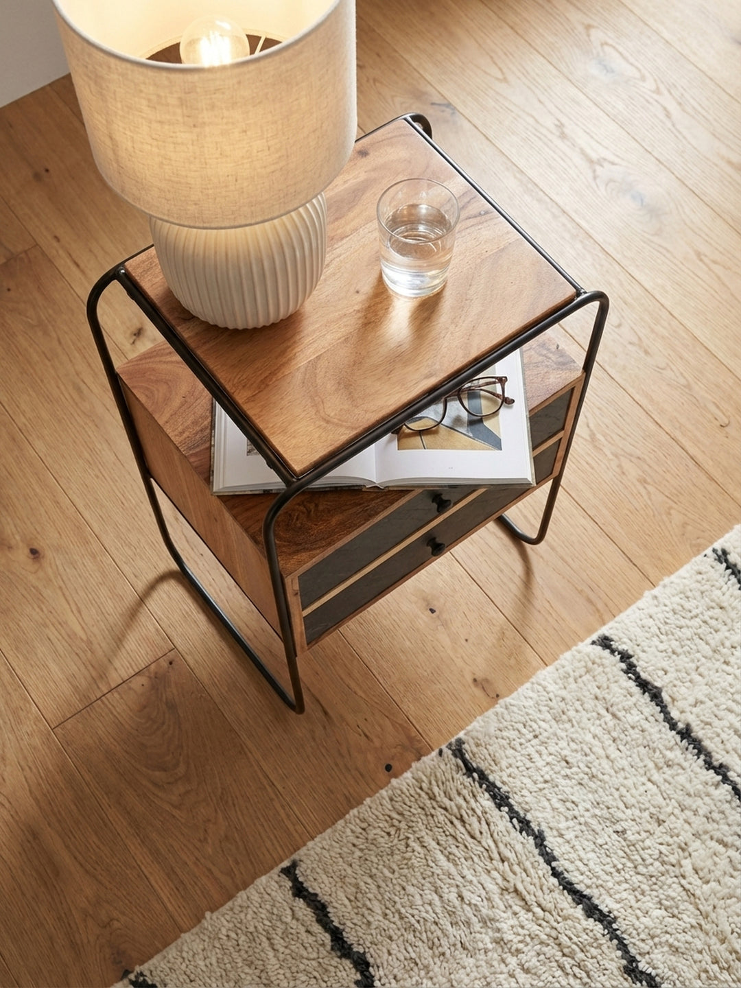 Nachttisch aus Holz und Metall von oben betrachtet, positioniert neben einem Boxspringbett auf einem cremefarbenen Beni Mrirt Teppich._