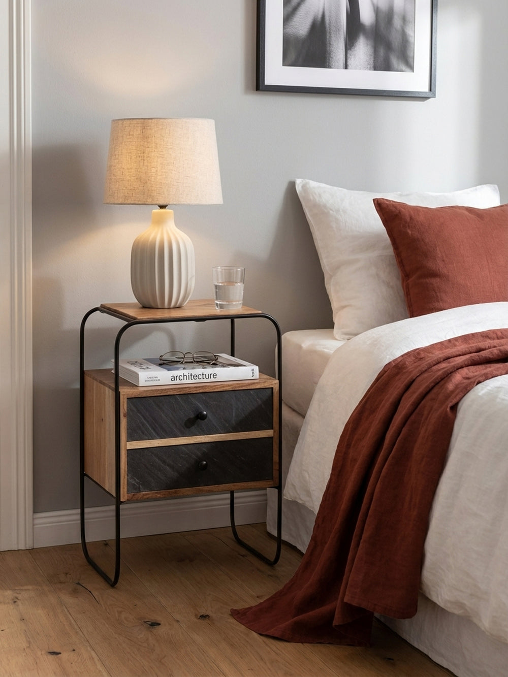 Nachttisch im Industrial-Stil mit einer modernen Tischlampe, Lesebrille und einem Buch als stilvolle Ablagefläche neben dem Bett._