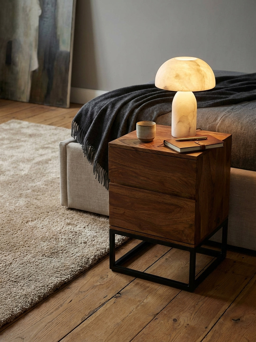 Design-Nachttisch mit einer leuchtenden Alabaster-Lampe und einem handgetöpferten Becher darauf._