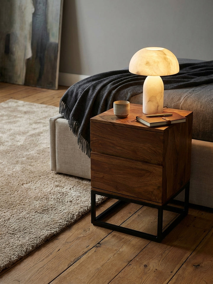 Design-Nachttisch mit einer leuchtenden Alabaster-Lampe und einem handgetöpferten Becher darauf._