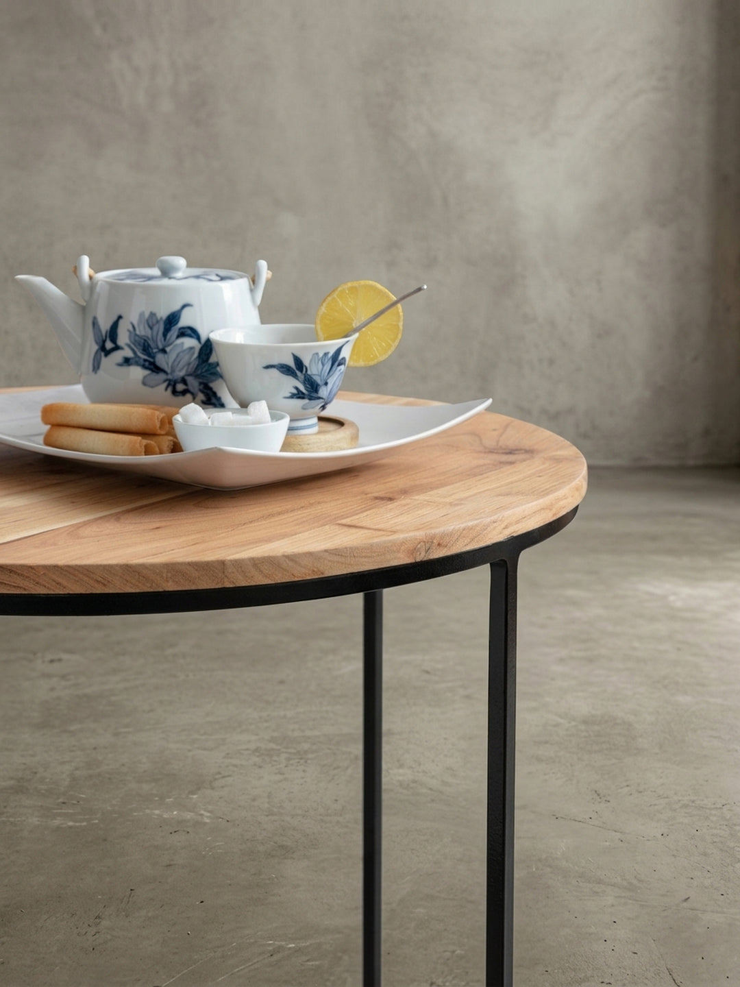 Makroaufnahme des Tischgestells. Die feine Pulverbeschichtung des 1 cm starken, schwarzen Metalls und der nahtlose Übergang zur massiven Akazienplatte des runden Sofatisches._