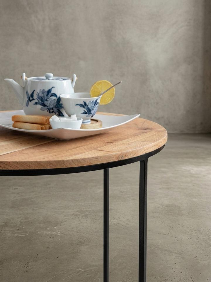 Makroaufnahme des Tischgestells. Die feine Pulverbeschichtung des 1 cm starken, schwarzen Metalls und der nahtlose Übergang zur massiven Akazienplatte des runden Sofatisches._