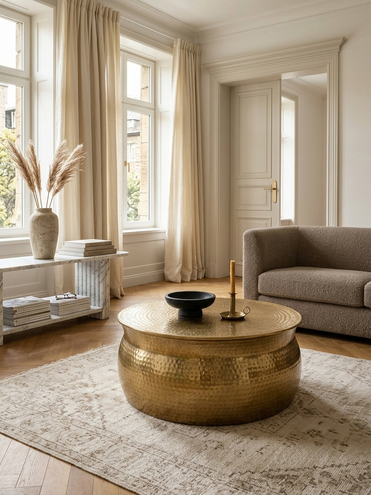 Aufsicht auf einen modernen Loungetisch in Gold, arrangiert auf einem hellen Teppich. Die gehämmerte Aluminiumoberfläche des 75 cm breiten Wohnzimmertisches wirkt edel._