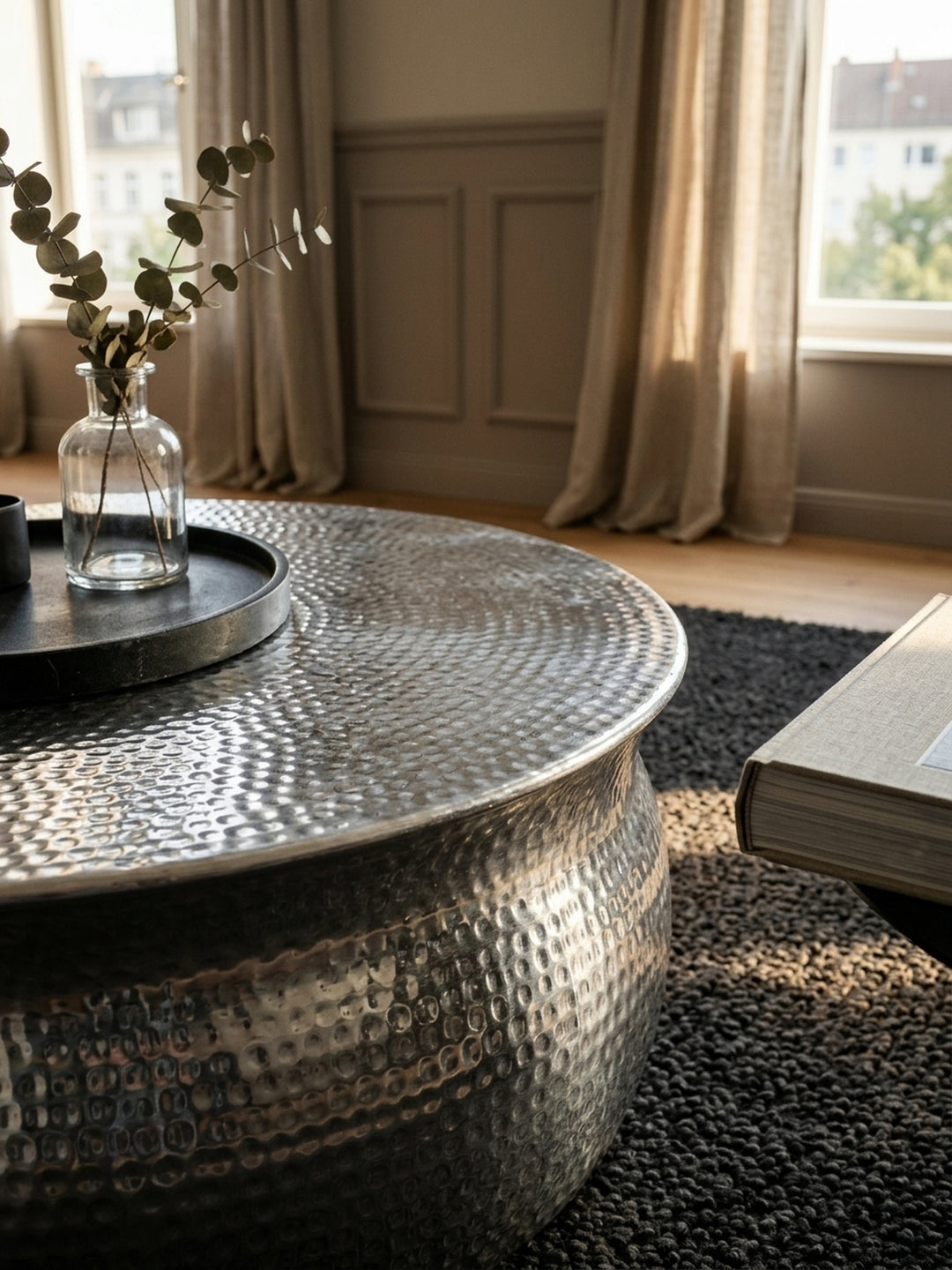 Nahaufnahme der handgefertigten Hammerschlag-Oberfläche des silbernen Couchtisches. Das strukturierte Aluminium sorgt für faszinierende Lichtreflexe und eine edle Haptik._