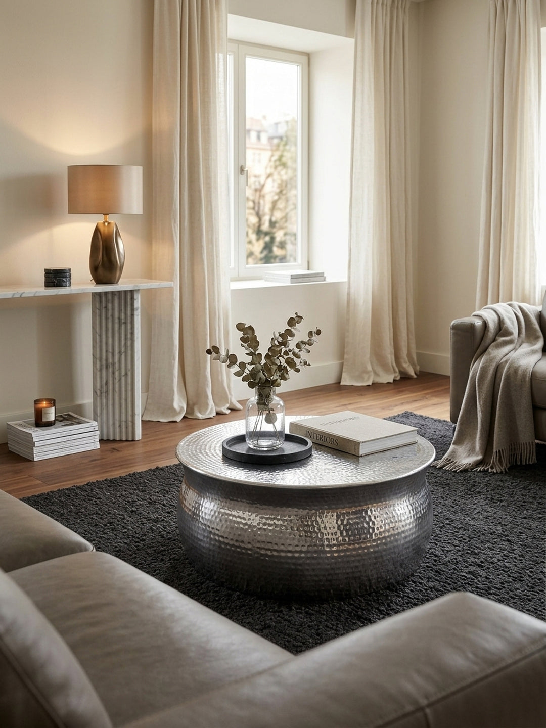 Eleganter Wohnbereich mit einem runden Couchtisch aus silbernem Aluminium. Das orientalische Hammerschlag-Design reflektiert warmes Licht im luxuriösen, modernen Wohnzimmer._