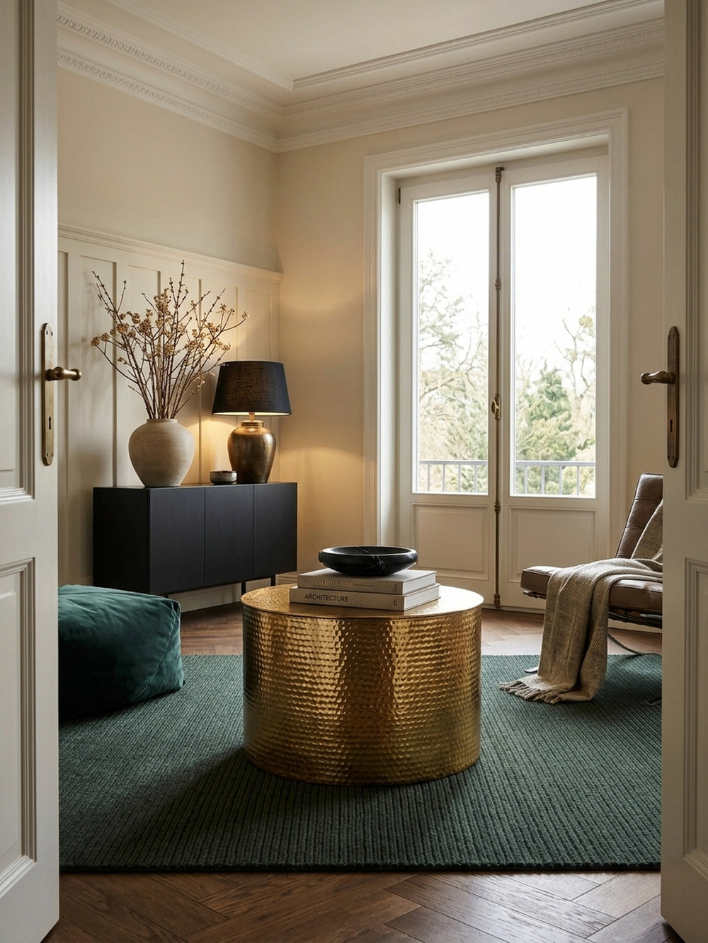 Eleganter runder Couchtisch aus goldenem Aluminium im luxuriösen Wohnzimmer. Der flache Wohnzimmertisch mit Hammerschlag-Design bildet ein glänzendes Zentrum auf dem dunklen Wollteppich._