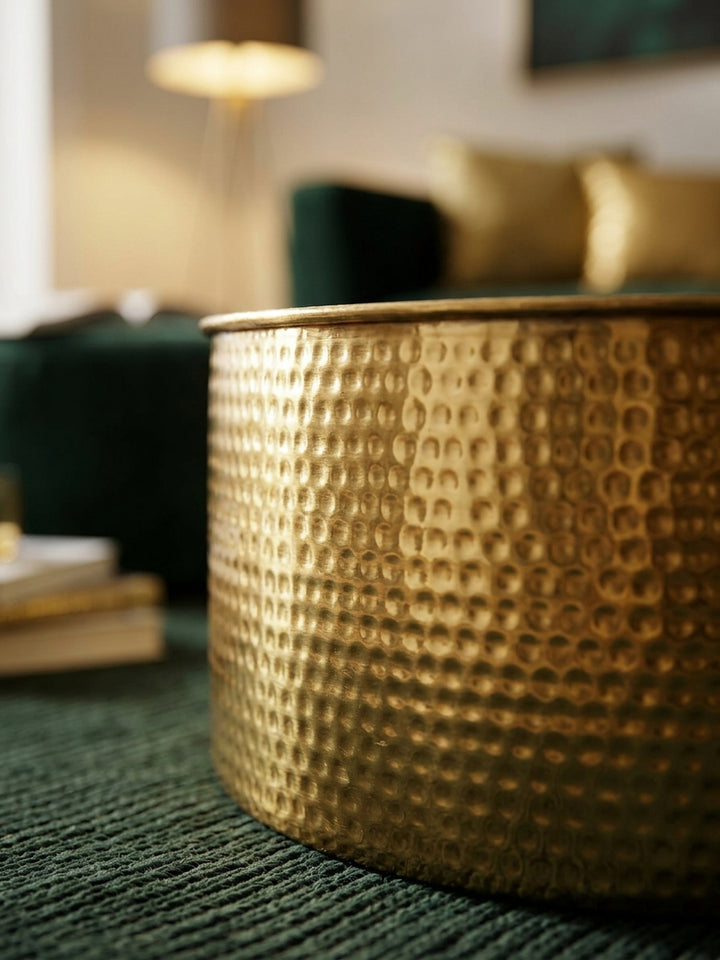 Nahaufnahme der handgefertigten Hammerschlag-Struktur des goldenen Sofatisches. Das glänzende Aluminium reflektiert das Licht und zeigt die feine, orientalisch anmutende Oberfläche._