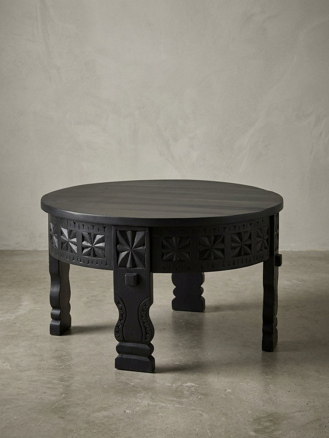 Freigestellter Design Couchtisch aus massivem Mangoholz, rund und schwarz lackiert, Frontansicht zeigt die kunstvollen Schnitzereien und die stabilen Beine._