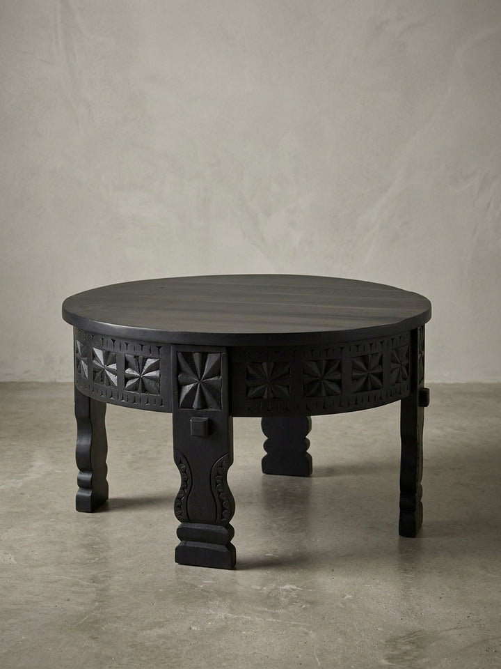 Freigestellter Design Couchtisch aus massivem Mangoholz, rund und schwarz lackiert, Frontansicht zeigt die kunstvollen Schnitzereien und die stabilen Beine._