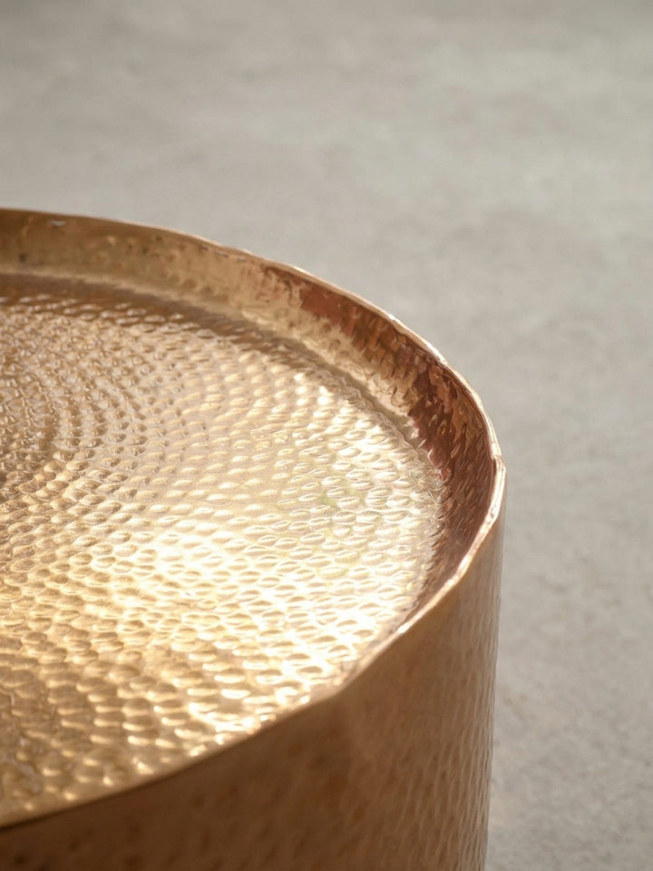 Makroaufnahme des erhöhten Randes und der detaillierten Hammerschlag-Struktur des goldenen Aluminium-Couchtischs für das Wohnzimmer._