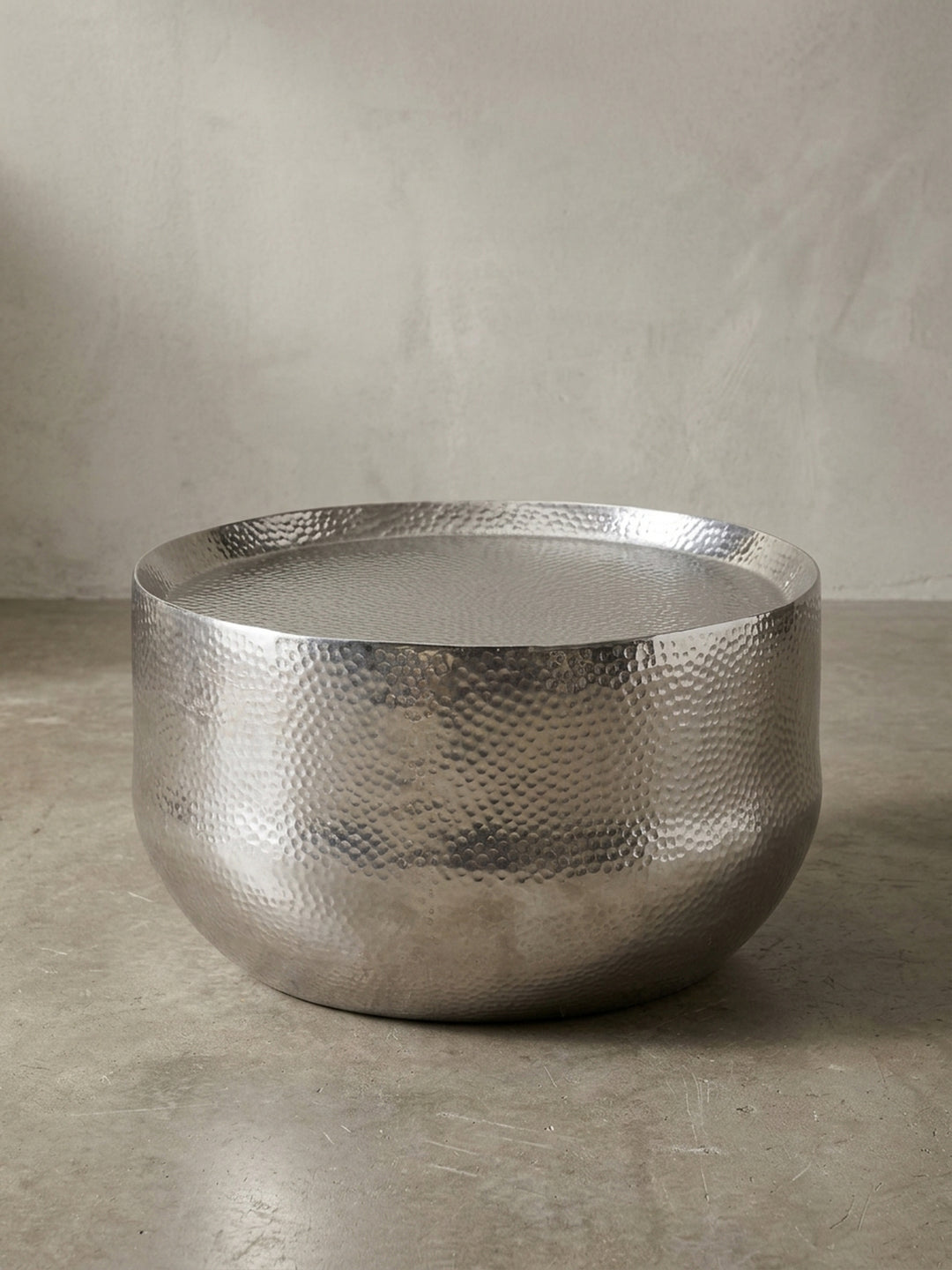 Designer Sofatisch aus Aluminium in Silber in der 3/4-Ansicht, die organische Form und die handgehämmerte Oberfläche sind deutlich erkennbar._