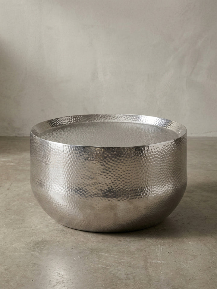 Designer Sofatisch aus Aluminium in Silber in der 3/4-Ansicht, die organische Form und die handgehämmerte Oberfläche sind deutlich erkennbar._