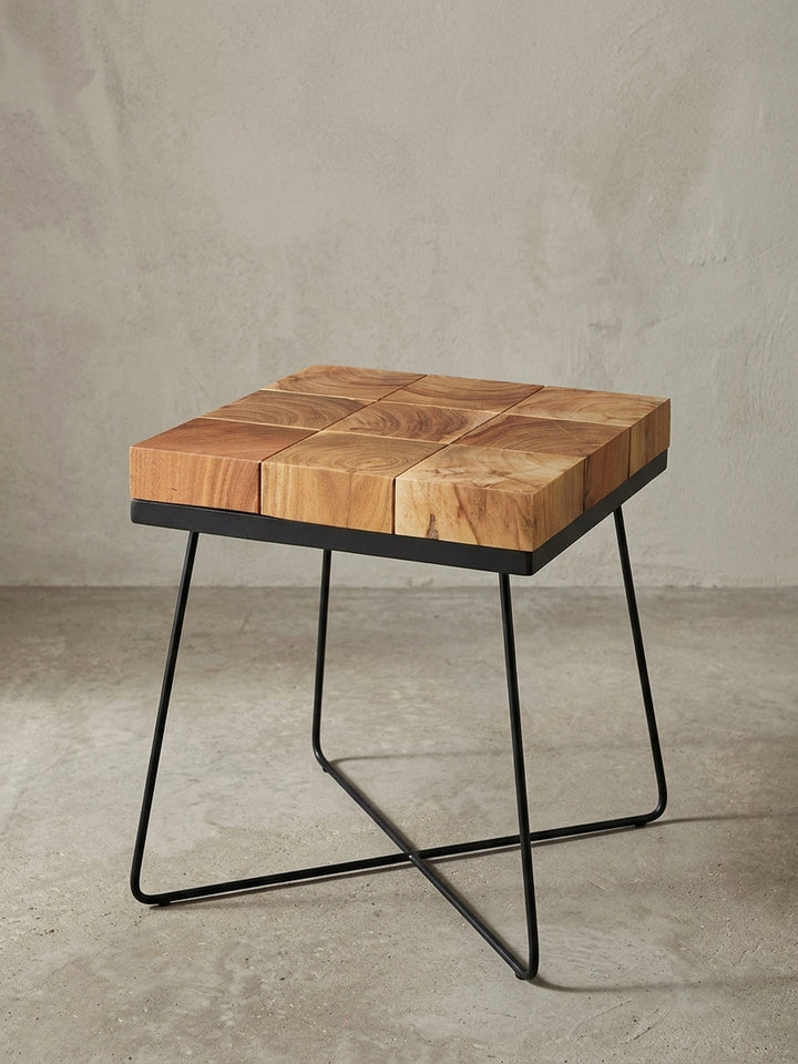 Quadratischer Anstelltisch in Frontalansicht mit einer markanten Massivholzplatte aus brauner Akazie und einem filigranen, mattschwarzen Metallkreuzgestell im Retro-Design._