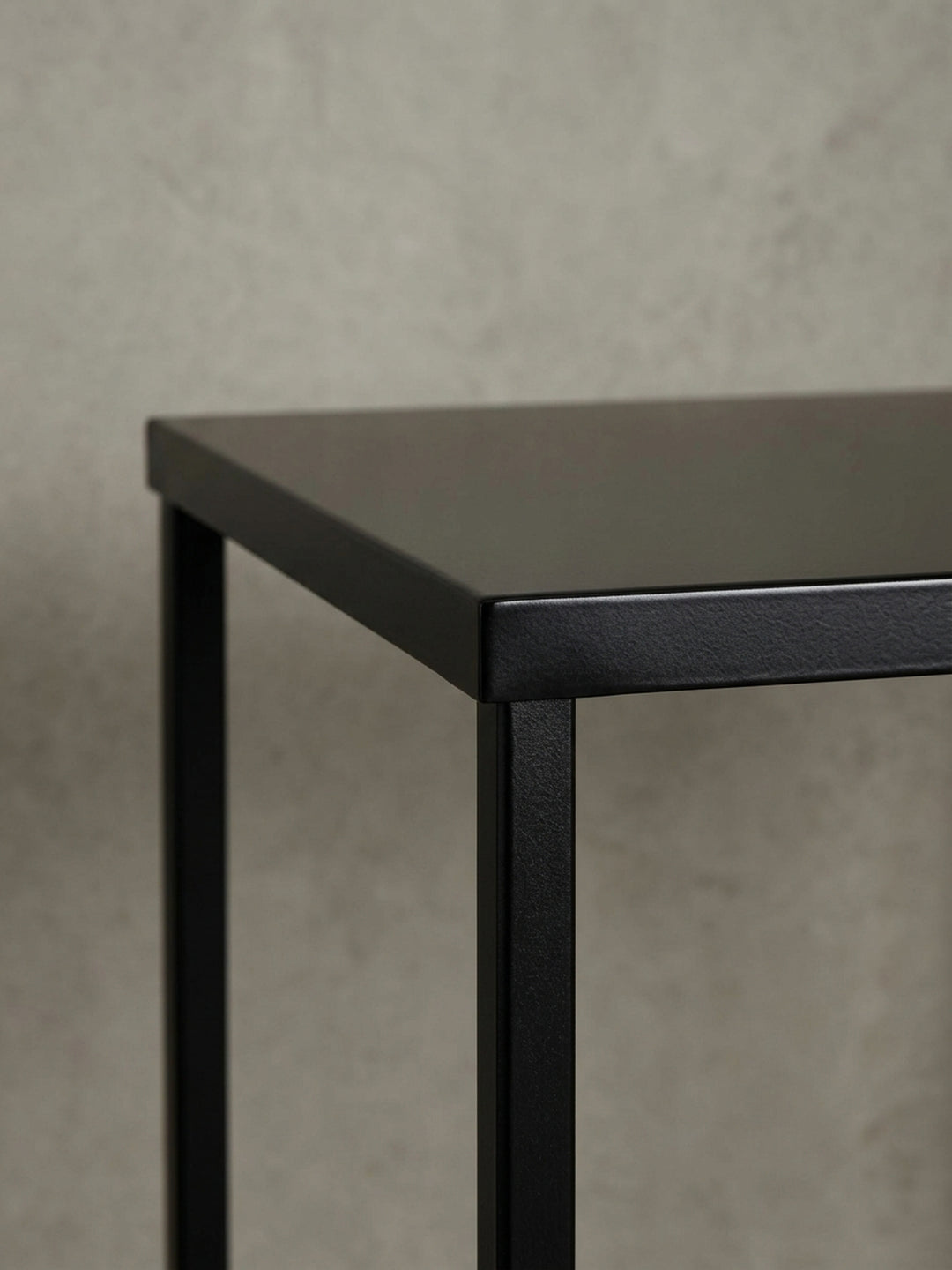 Eine alternative Perspektive auf den Kaffeetisch, die das Zusammenspiel von Licht und Schatten auf der mattschwarzen Oberfläche und dem offenen Gestell betont._