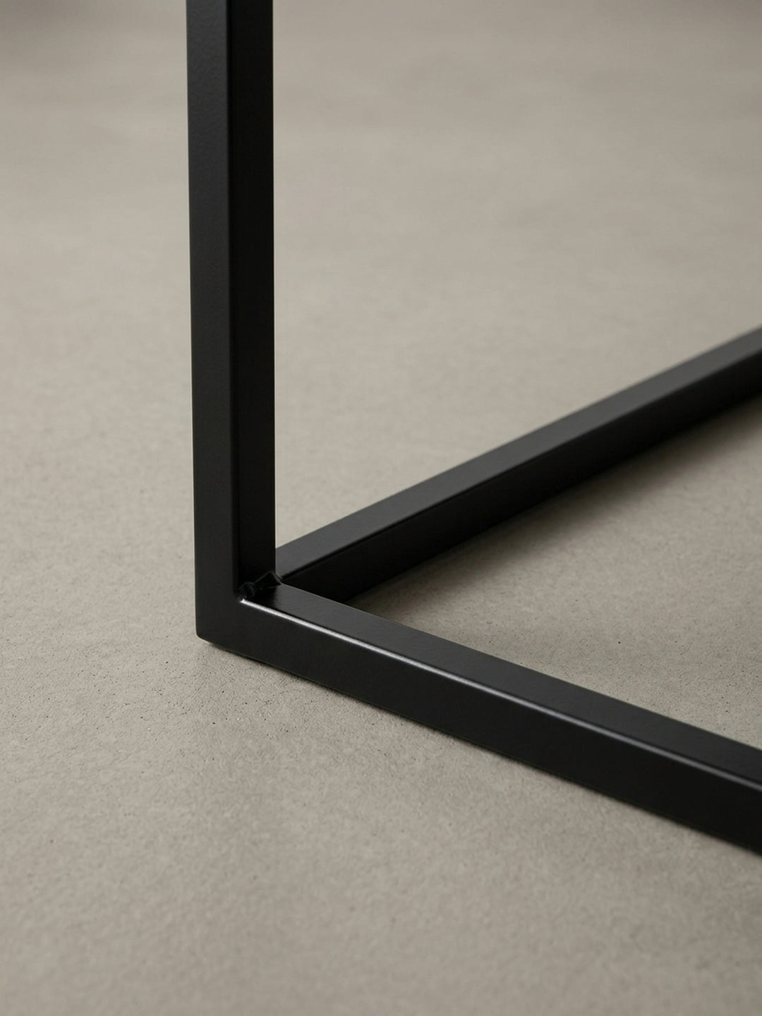 Detailaufnahme einer Ecke des schwarzen Couchtisches, die die präzise Kantenverarbeitung der Tischplatte und den Übergang zum 1,5 cm starken Stahlgestell fokussiert._