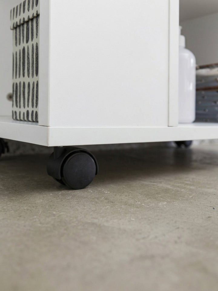 Gesamtübersicht des geometrischen Bücherregals in strahlendem Weiß. Klare Linien und der Mix aus offenen Fächern machen den Rollwagen zum perfekten Begleiter neben dem Schreibtisch._