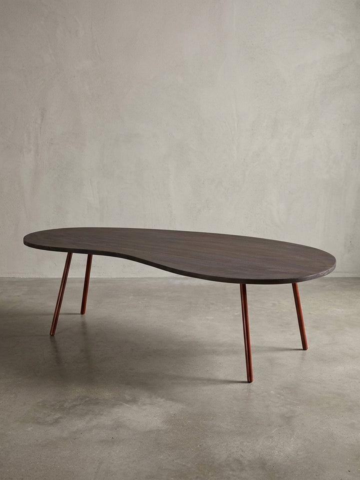 Gesamtansicht des extravaganten Nierentisches auf weißem Hintergrund. Der 122x63cm große Couchtisch verbindet Retro-Charme mit hochwertigen Materialien wie massivem Akazienholz._