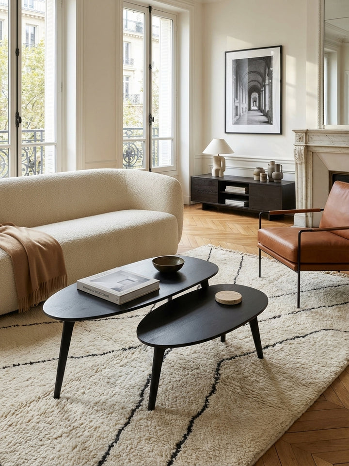 Das zweiteilige Couchtisch-Set in Schwarz ergänzt elegant ein hellgraues Bouclé-Sofa und schafft eine moderne, organisch inspirierte Wohnatmosphäre._