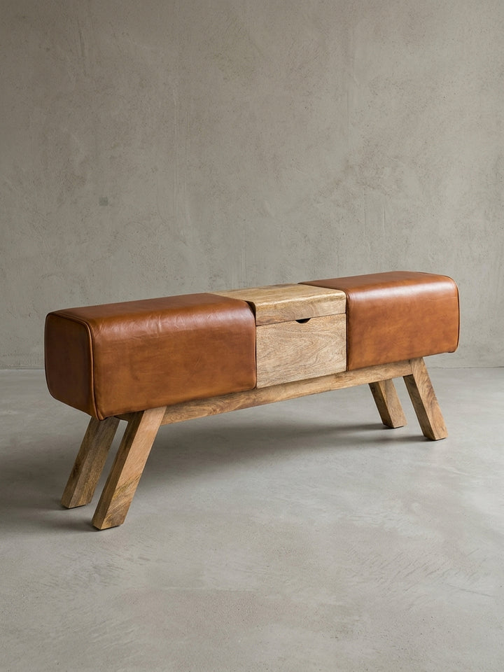 Vorderansicht der Design Turnbock Sitzbank. Braunes Echtleder, mittiges Holzfach und vier schräge Holzbeine aus Mangoholz zeigen die markante 120x53cm Silhouette im Turnhocker-Stil._