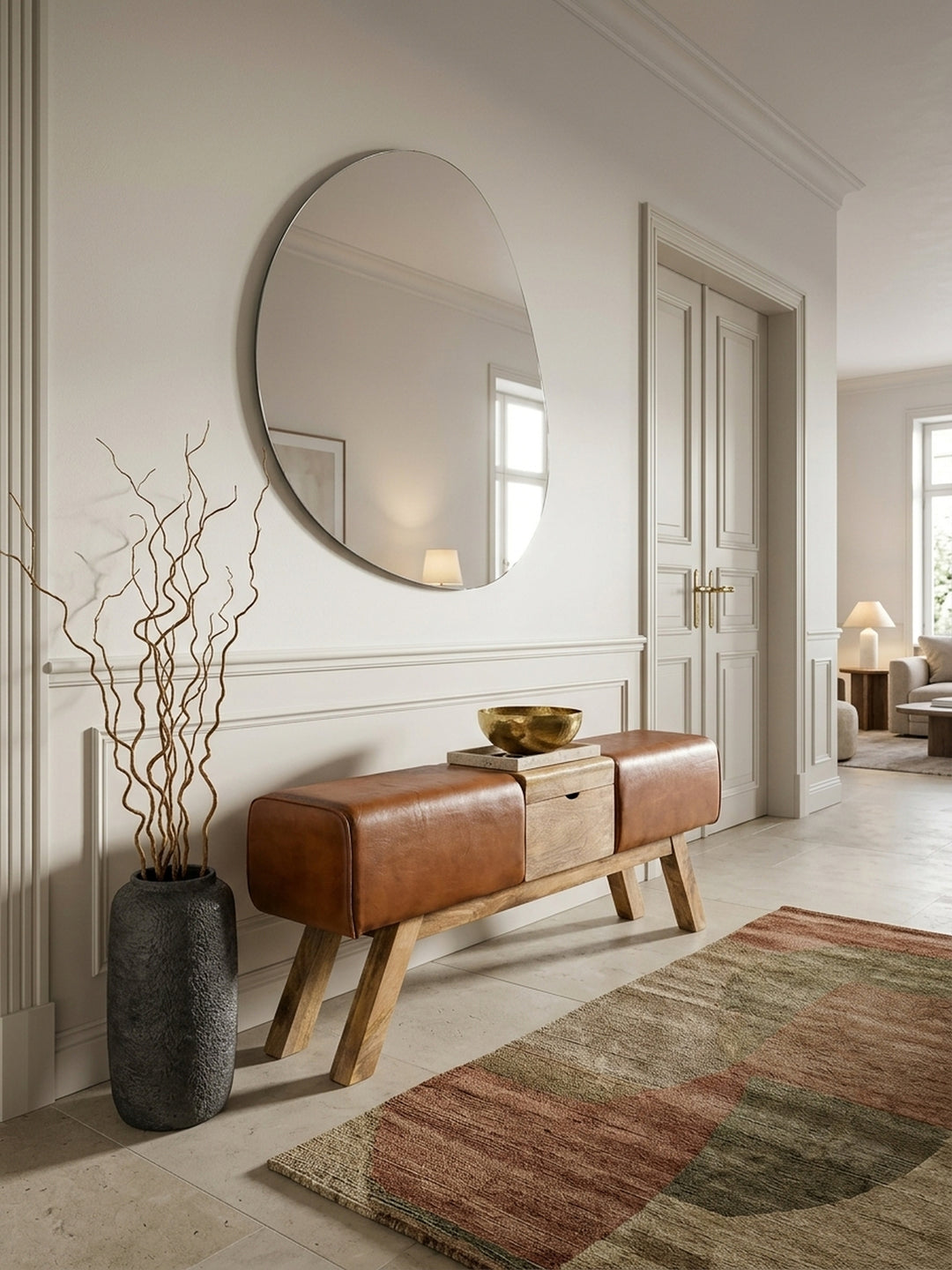 Elegante Turnbock Sitzbank im Eingangsbereich, 120x29x53cm. Braunes Echtleder und massives Mangoholz harmonieren in einem luxuriösen Flur mit Natursteinboden und asymmetrischem Spiegel._