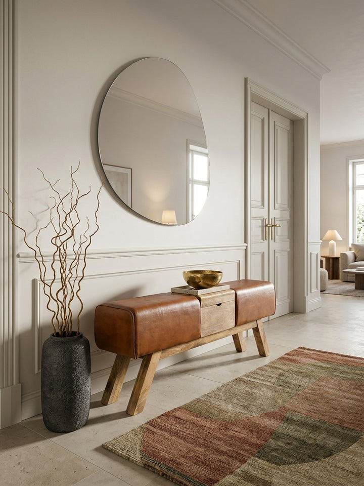 Elegante Turnbock Sitzbank im Eingangsbereich, 120x29x53cm. Braunes Echtleder und massives Mangoholz harmonieren in einem luxuriösen Flur mit Natursteinboden und asymmetrischem Spiegel._