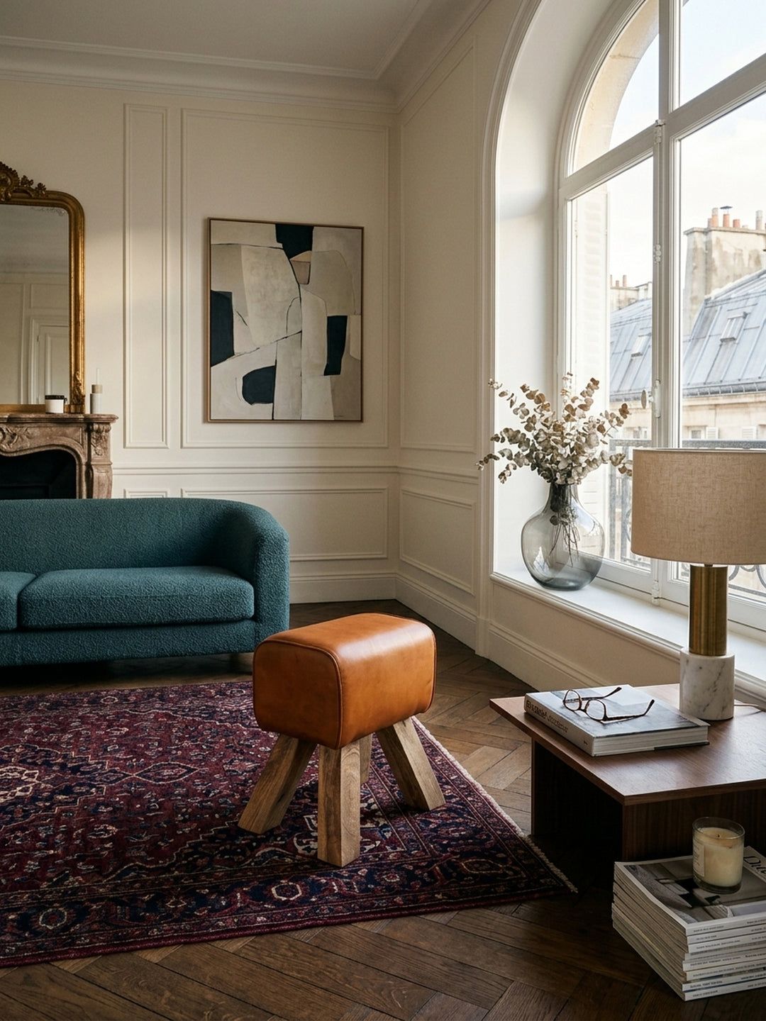 Design Turnbock Sitzhocker aus braunem Echtleder im eleganten Wohnzimmer. Der kompakte Hocker mit Massivholz-Beinen dient als stilvolle Vintage-Sitzgelegenheit neben einer Leseecke._