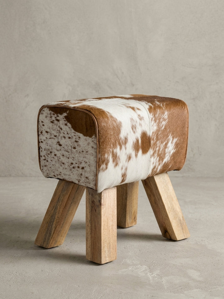Eine alternative Perspektive auf den Country-Look Hocker fokussiert das lebendige Farbenspiel von warmen Erdtönen und reinem Weiß im natürlichen Fell-Design._