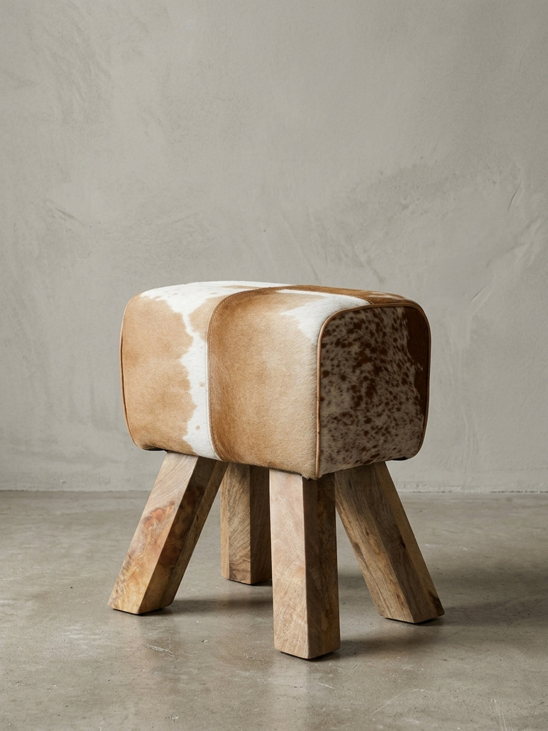 Freigestellt präsentiert sich der Design Turnbock Sitzhocker mit seiner einzigartigen Kuhfell-Musterung und den vier schräg stehenden, stabilen Holzbeinen._