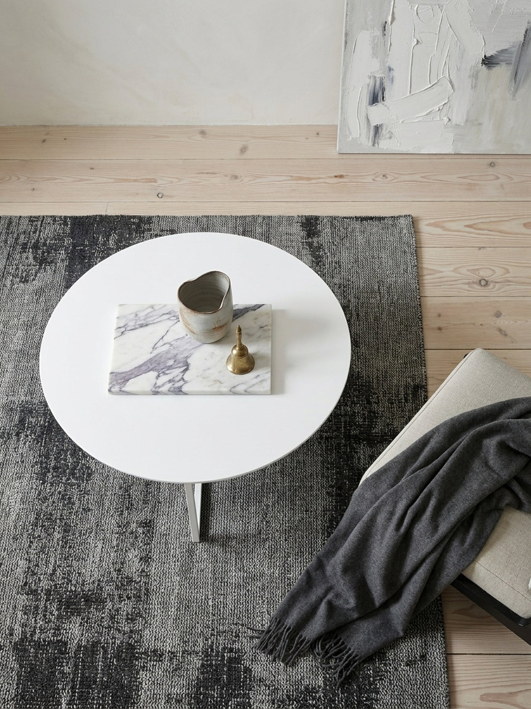 Draufsicht auf den runden Kaffeetisch mit 80cm Durchmesser in mattweißem Finish arrangiert mit gemütlichen Sesseln auf einem handgewebten dunkelgrauen Wollteppich._