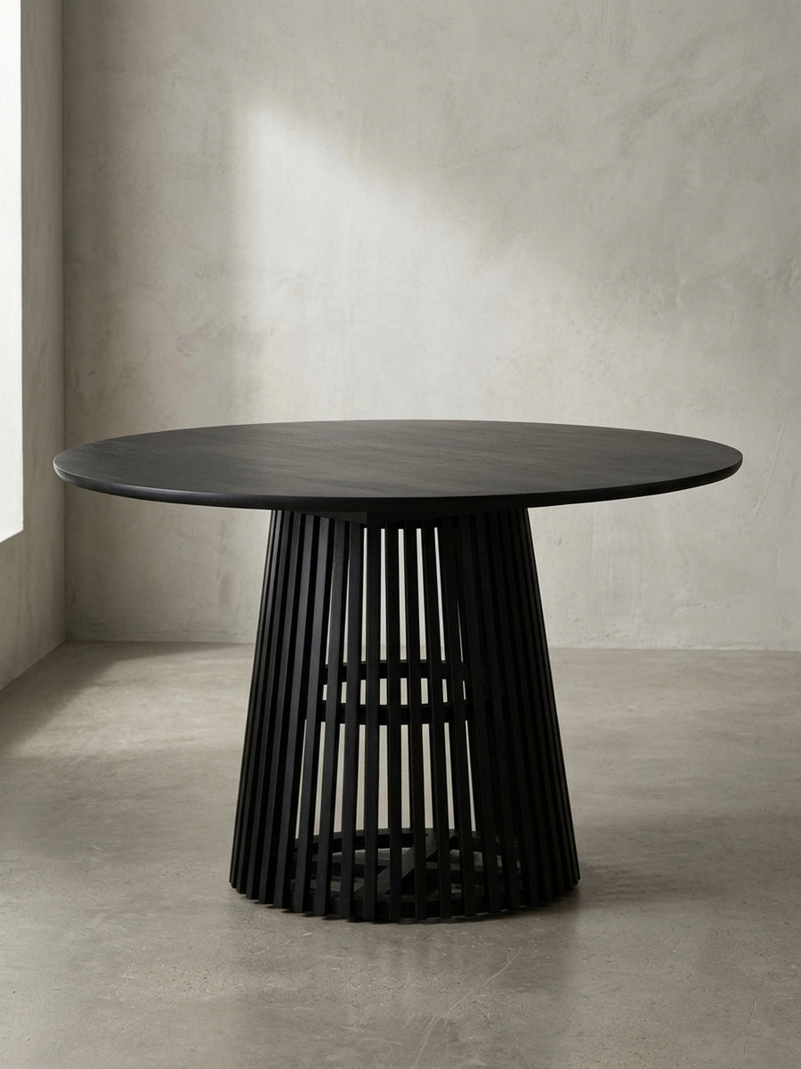 Frontalansicht des modernen Esstischs aus massivem Mangoholz in Schwarz, der das skulpturale Gittergestell und die runde Tischplatte zeigt._