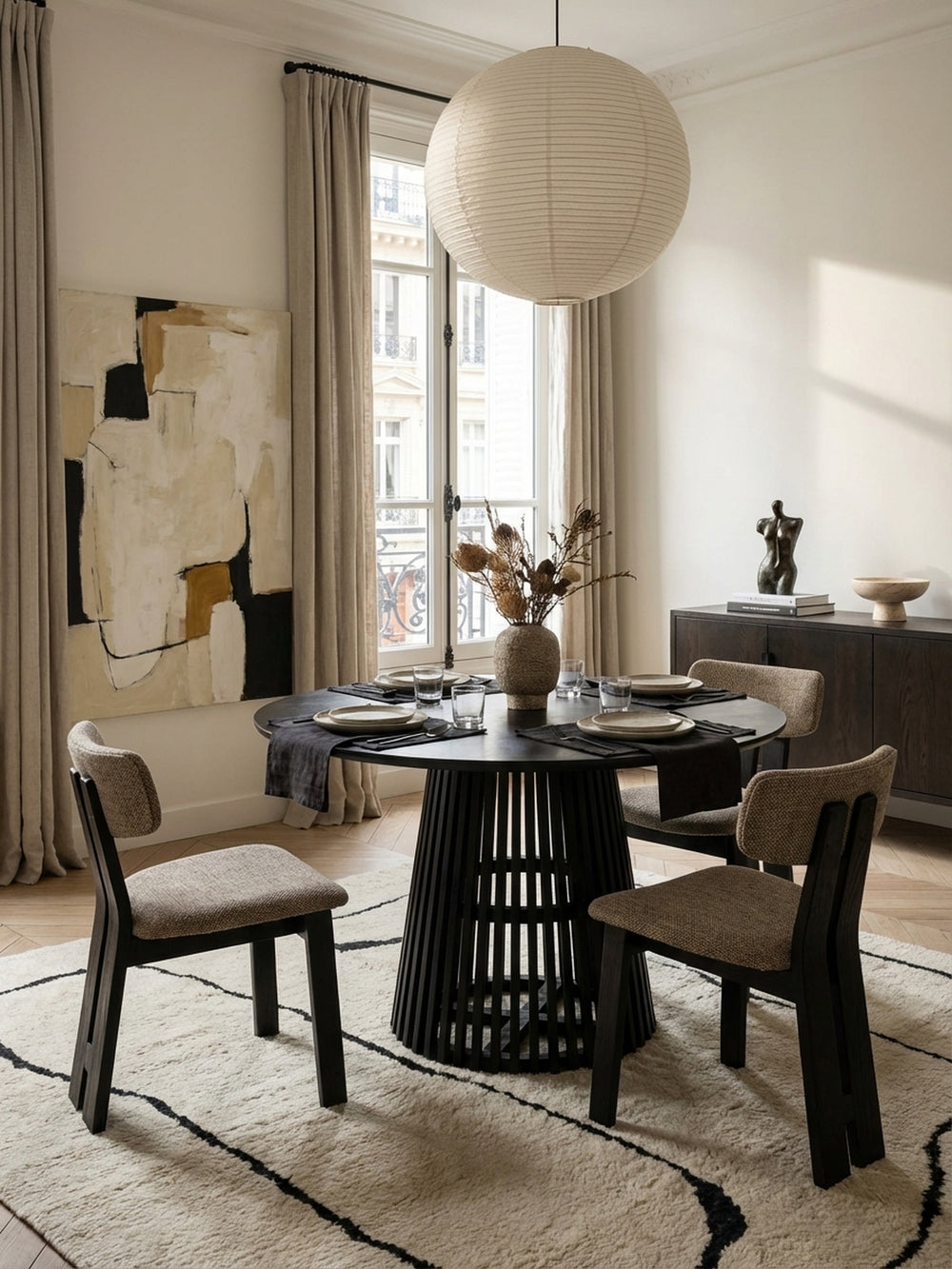 Der runde Küchentisch aus massivem Mangoholz kombiniert mit minimalistischen Esszimmerstühlen aus grauem Stoff vor einem großen Fenster._