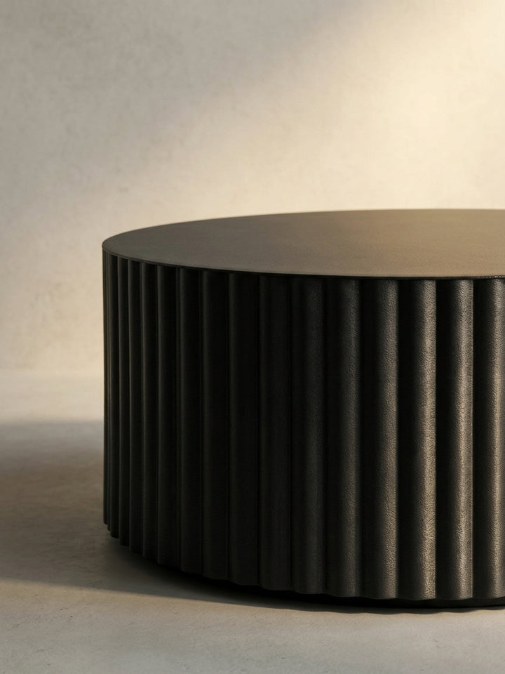 Der runde Couchtisch in Schwarz aus einer dynamischen Perspektive, die das Spiel von Licht und Schatten auf dem Wellen-Muster einfängt._