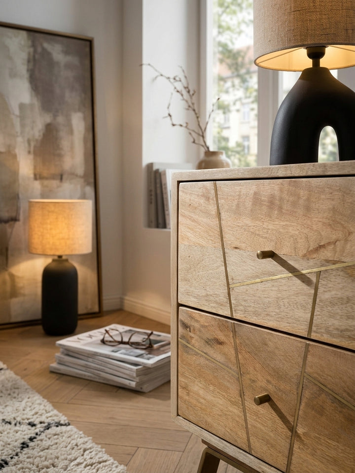 Detailaufnahme der Mangoholz Oberfläche des Nachttisches. Sichtbare Holzmaserung, goldfarbene Metallstreifen und ein filigraner Griff an der Schublade der Nachtkonsole._