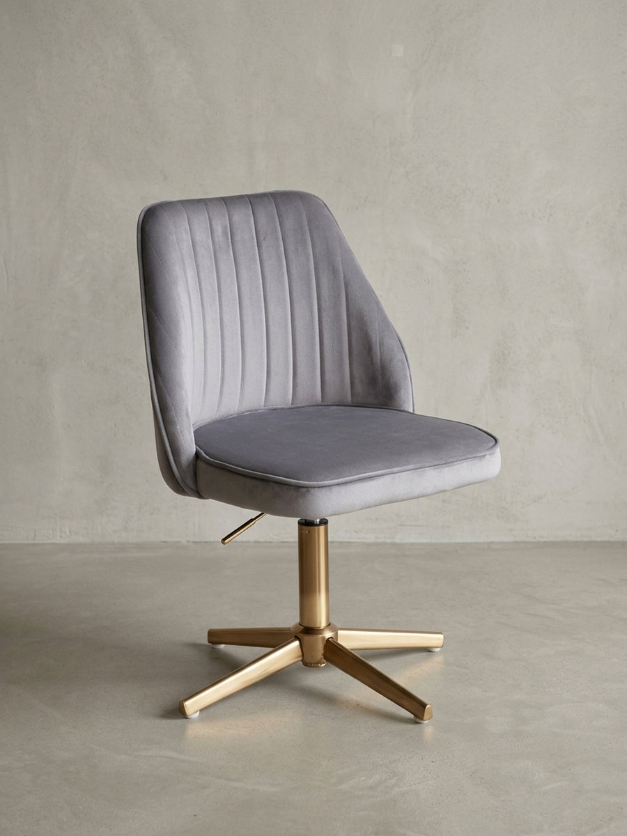 Grauer Samt-Schreibtischstuhl mit goldenem Drehgestell, Frontansicht auf weißem Hintergrund, zeigt die gesteppte Rückenlehne und die Sitzschale._