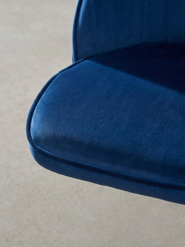 Detailaufnahme des goldenen Vierfuß-Drehgestells des blauen Samtstuhls. Die hochwertige Lackierung und die stabilen Füße des Arbeitsstuhls werden in Nahaufnahme gezeigt._