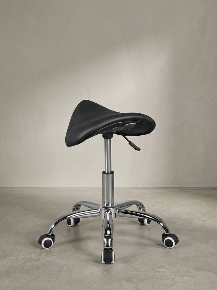 Draufsicht leicht schräg auf den ergonomischen Sattelstuhl, die charakteristische Sitzmulde für viel Beinfreiheit und die verchromten Rollen fallen auf._