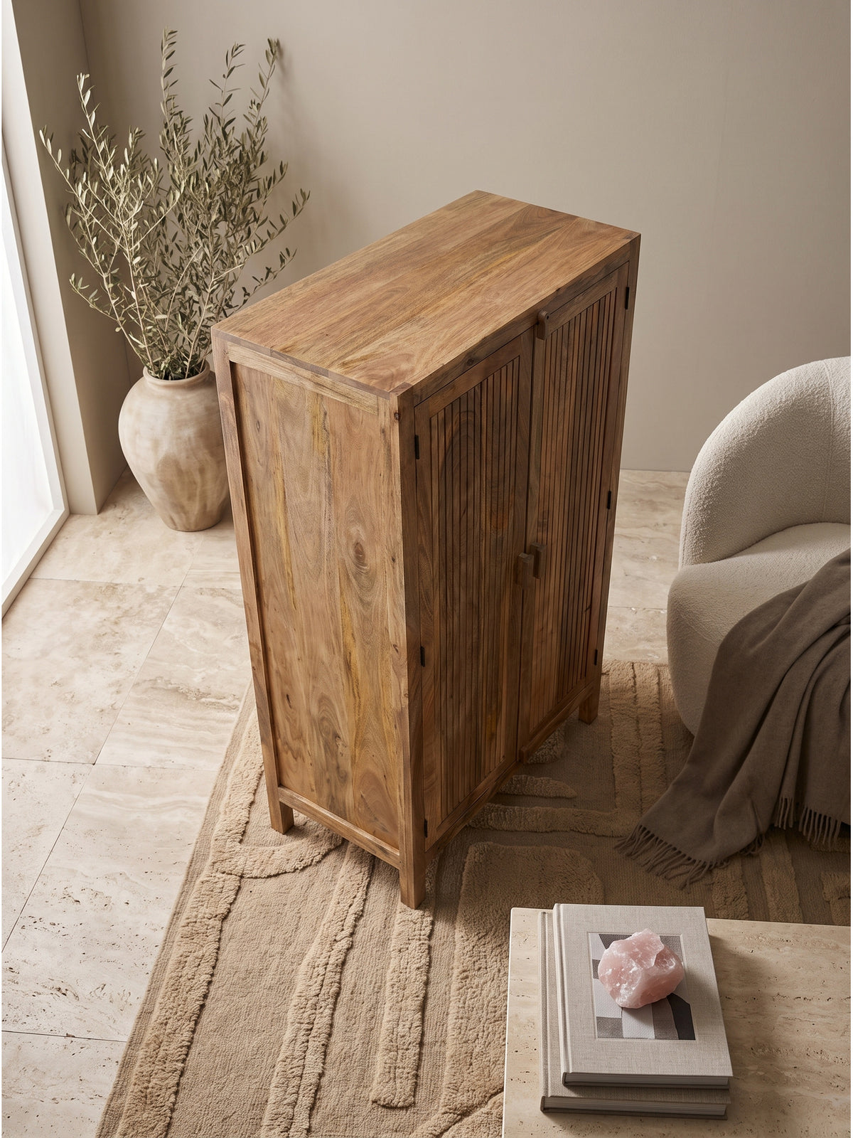 Ansicht von oben auf den naturfarbenen Holzschrank 90x44x187 cm, der neben einem beigen Bouclé-Sessel und einer großen Keramikvase steht.