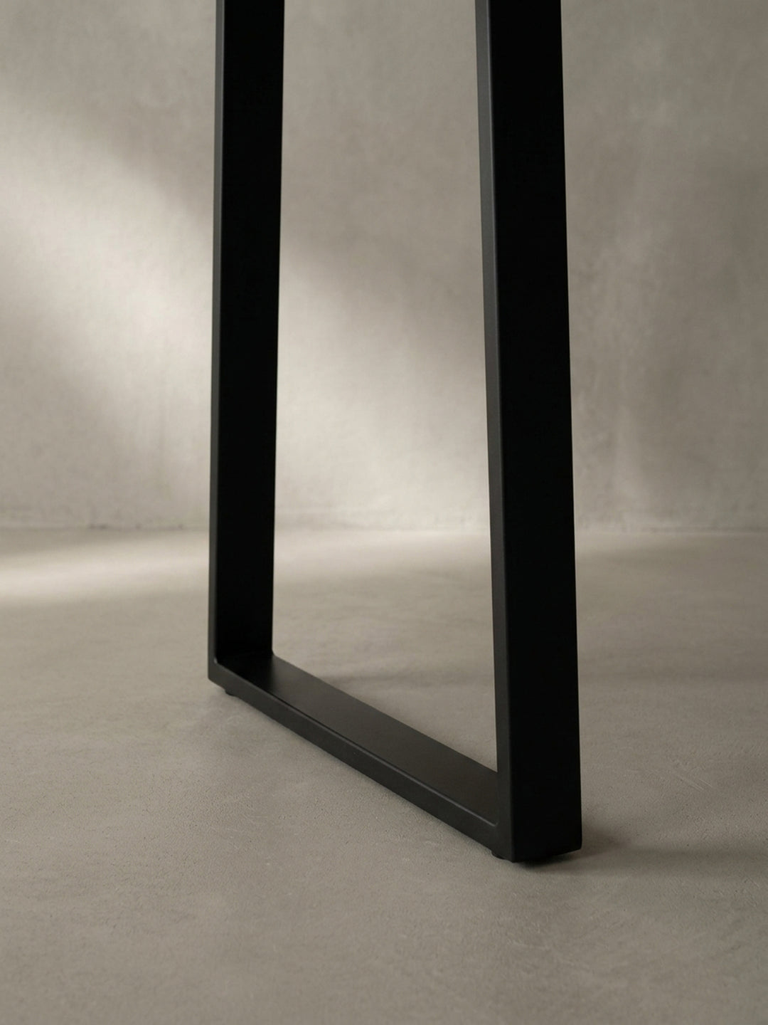 Detailaufnahme des schwarzen, pulverbeschichteten Trapezbeins, das die hochwertige Verarbeitung und die moderne, geometrische Form des Metallgestells zeigt._
