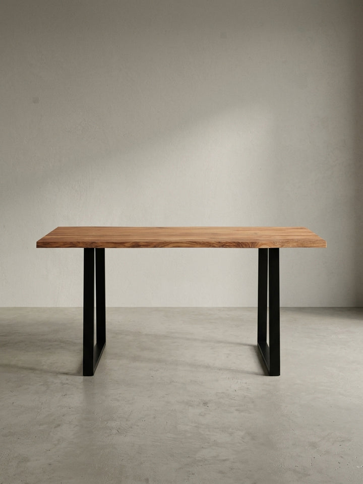 Frontalansicht des Schreibtisches aus massivem Akazienholz mit einer 200 cm breiten Tischplatte mit Baumkante und robusten, schwarzen Metall-Trapezbeinen._