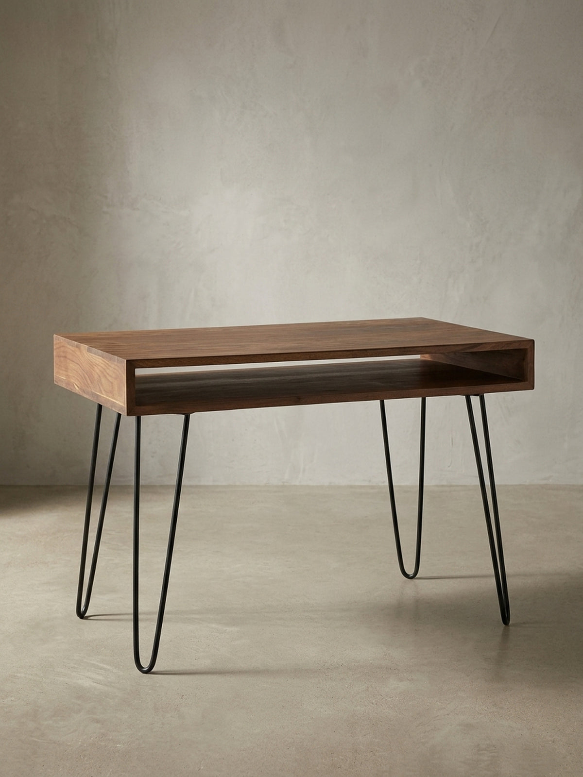 Schreibtisch aus warmem Sheesham-Massivholz mit markanter Maserung auf neutralem Betonhintergrund Frontalansicht 60x110x76 cm