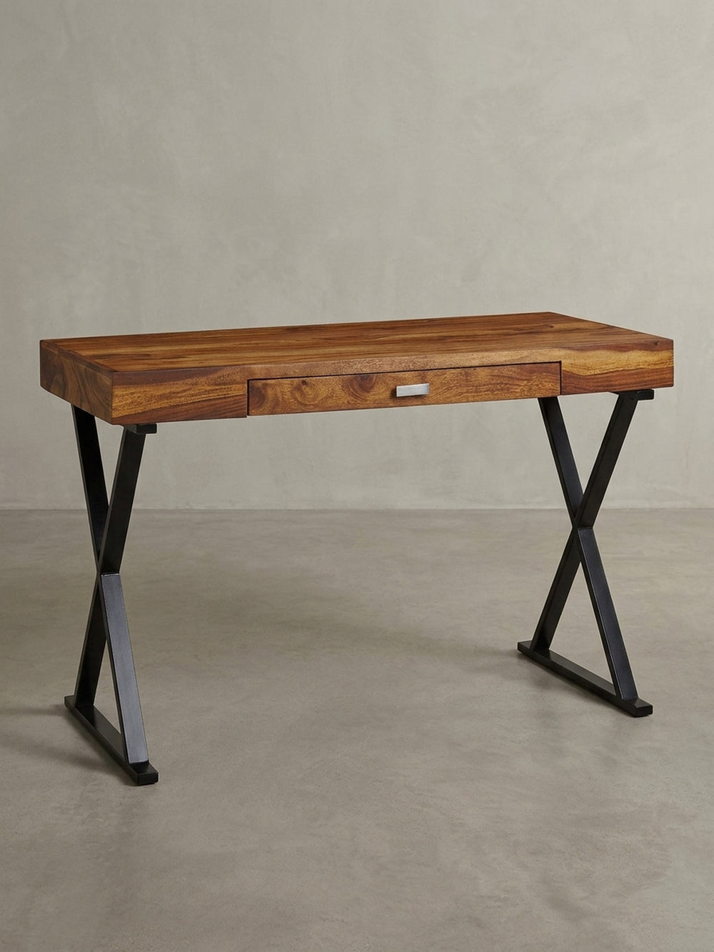 Industrie-Design Schreibtisch in einer 3/4-Ansicht, die die Tiefe der 55 cm Tischplatte aus Sheesham Holz und die stabile Konstruktion der schwarzen X-förmigen Beine zeigt._