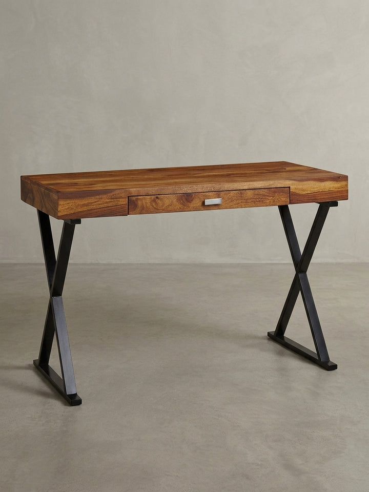 Industrie-Design Schreibtisch in einer 3/4-Ansicht, die die Tiefe der 55 cm Tischplatte aus Sheesham Holz und die stabile Konstruktion der schwarzen X-förmigen Beine zeigt._