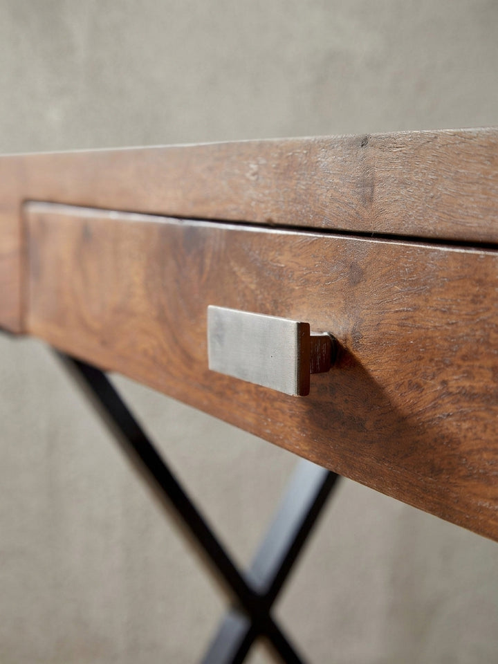 Design Bürotisch mit praktischer Schublade und stabilen X-Beinen, eine alternative Perspektive, die die Balance zwischen dem warmen Holz und dem kühlen Metall betont._