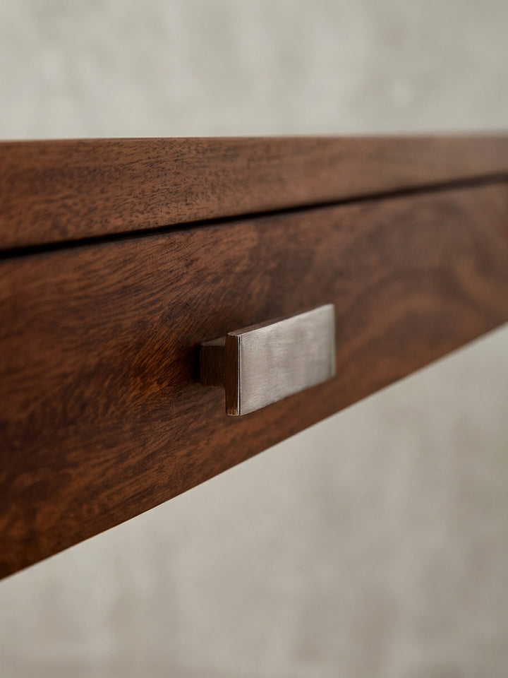 Nahaufnahme des schlichten, rechteckigen Griffs aus gebürstetem Metall an der Schublade des Massivholz-Schreibtisches._