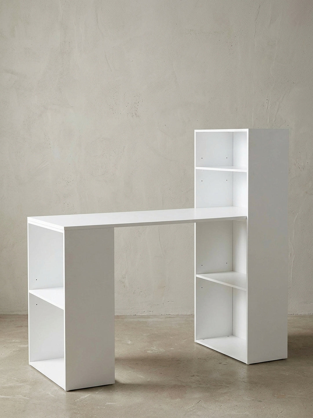 Moderner Schreibtisch mit integriertem Regal in mattem Weiß vor neutralem Hintergrund. Frontalansicht zeigt die asymmetrische Form mit 53 cm Tiefe und viel Stauraum._