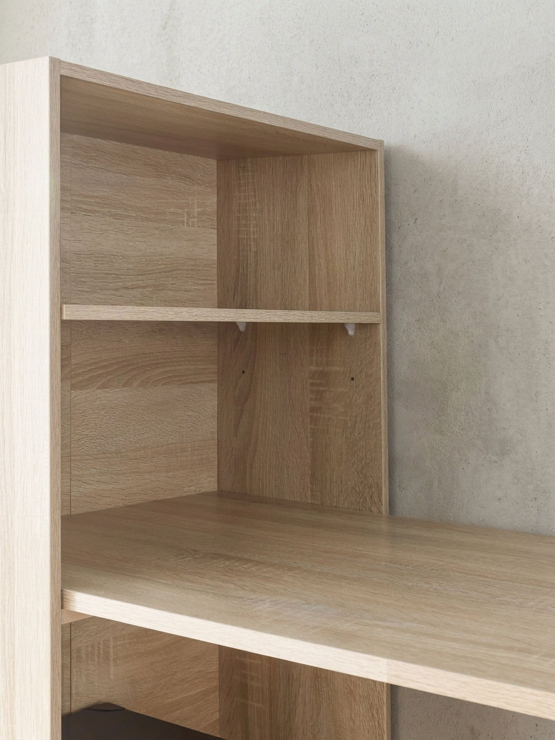 Nahaufnahme der Verbindungsstellen zwischen Arbeitsplatte und Regalteil. Die saubere Verarbeitung der Spanplatte im Eichendekor unterstreicht das minimalistische, moderne Möbeldesign._