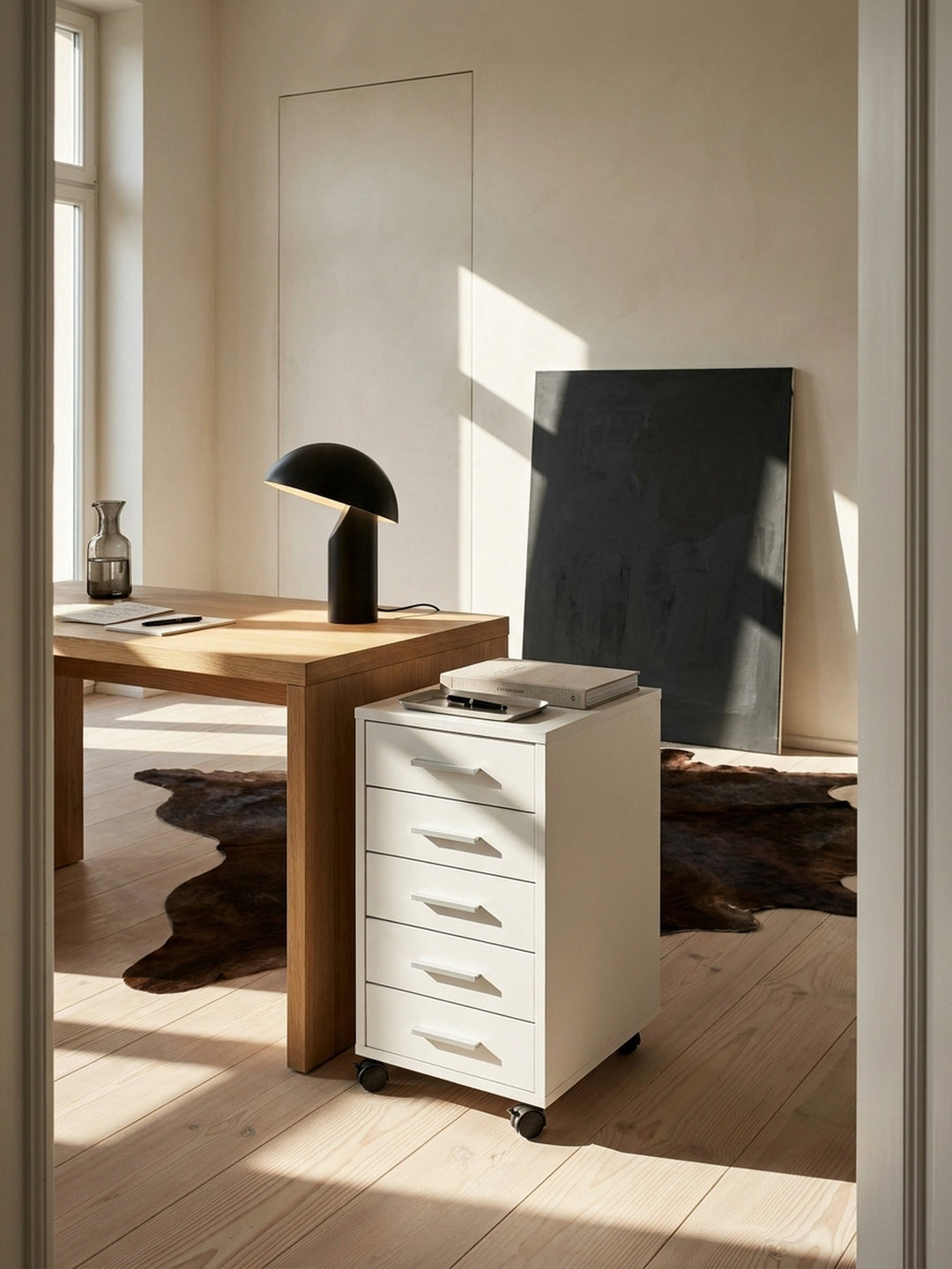 Eleganter Rollcontainer in mattem Weiß mit fünf Schubladen arrangiert im minimalistischen Home Office neben einem massiven Holzschreibtisch._