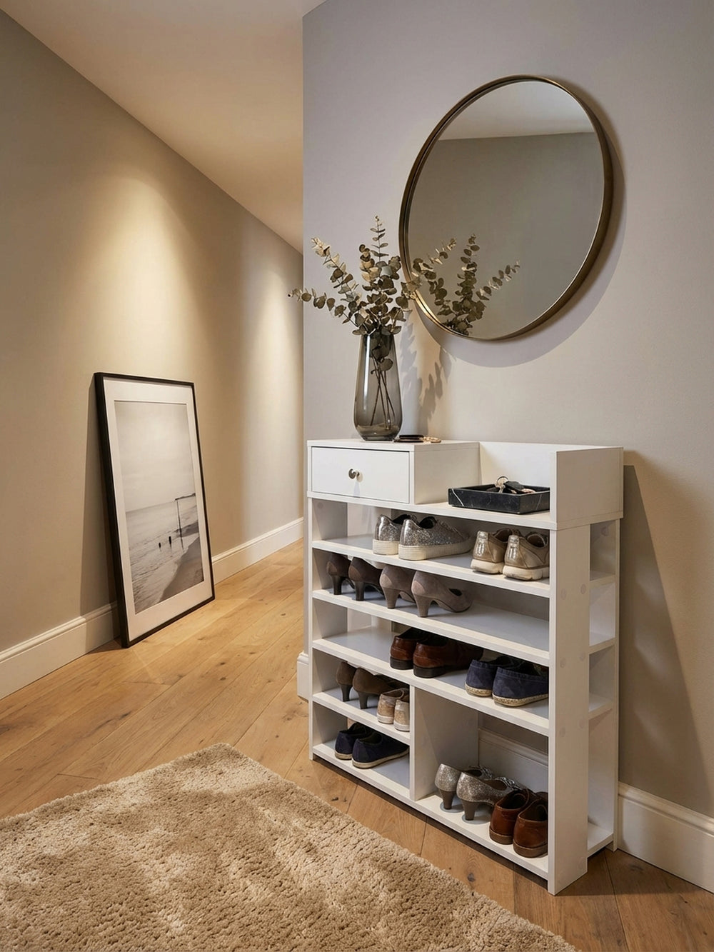 Das weiße Schuhregal mit 75 cm Breite im eleganten Flur, stilvoll dekoriert mit Spiegel und Kunst, schafft eine organisierte und einladende Atmosphäre im Eingangsbereich._